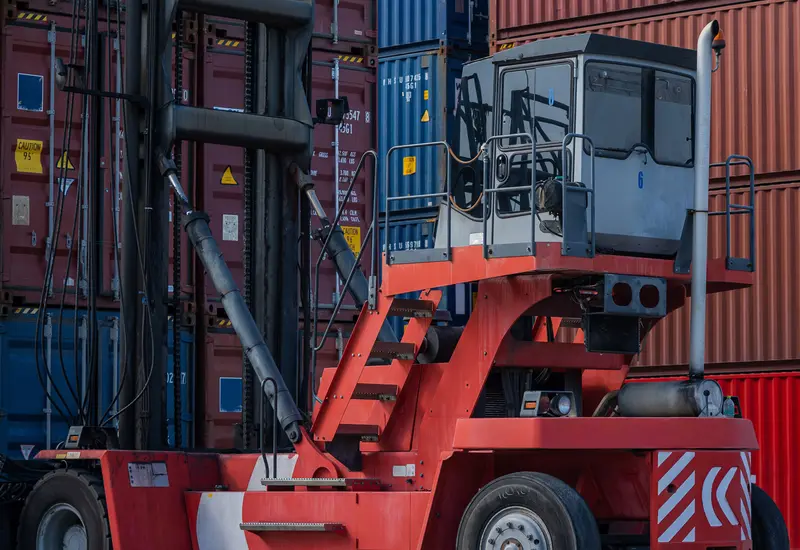 Red reach stacker in a container yard in front of stacked red and blue containers
